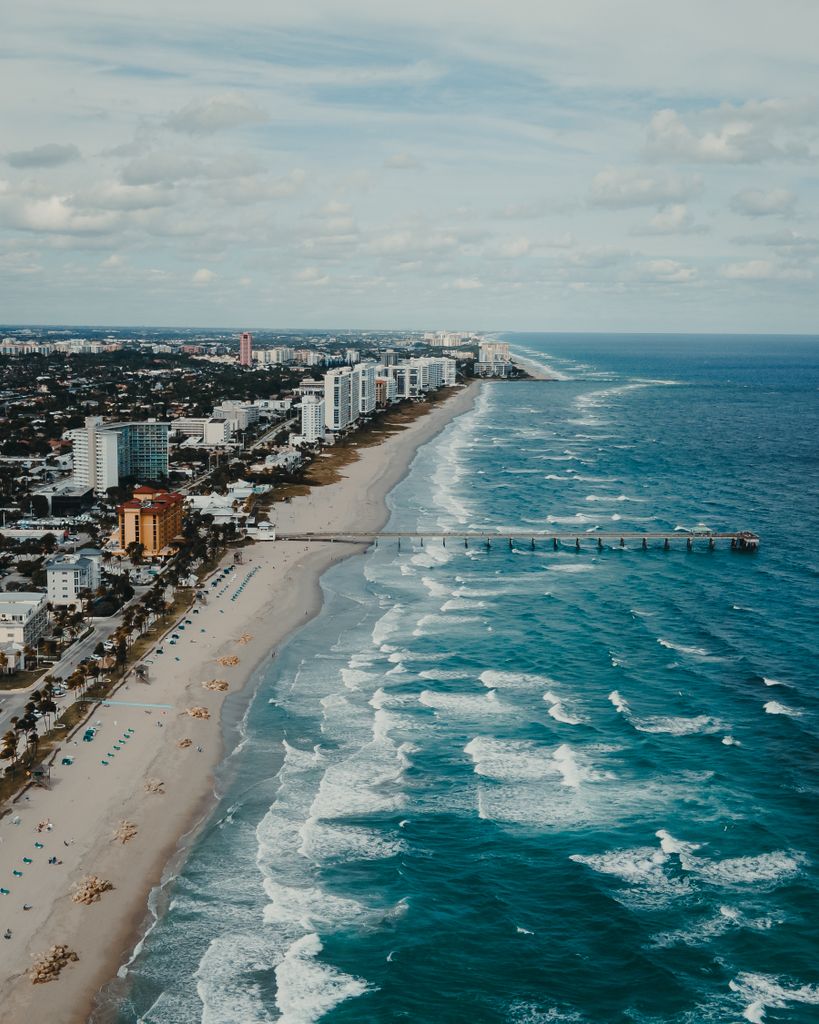 A stunning aerial view of a beachfront cityscape with a long pier and turquoise waves.